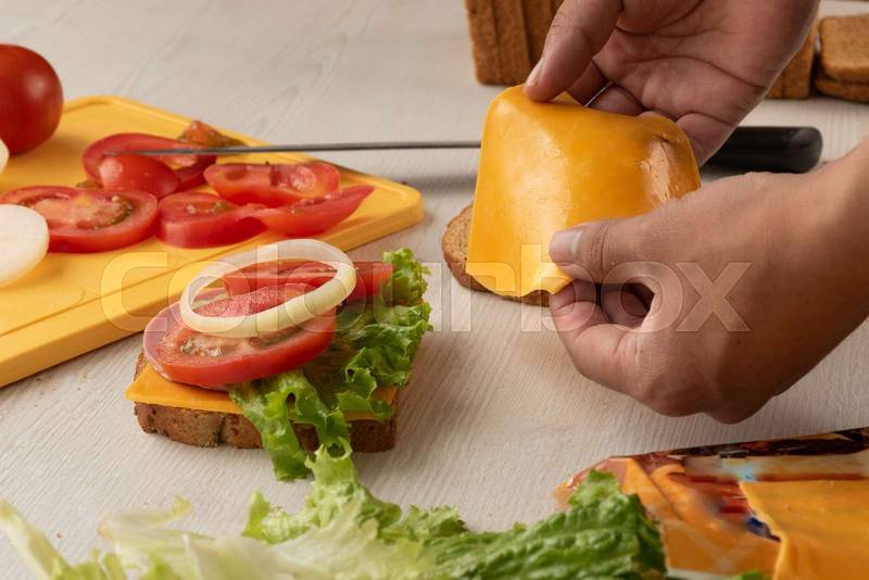 preparing and placing the cheddar cheese of a delicious sandwich with lettuce, fresh tomato and onion rings on a table
