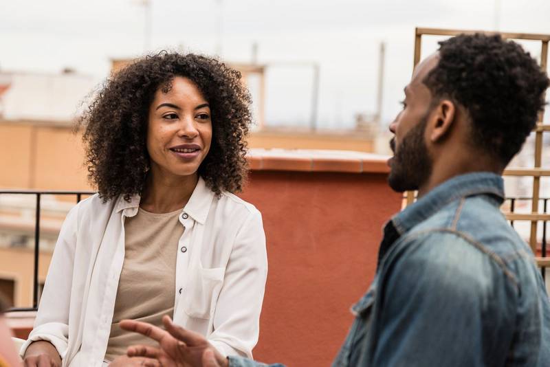 Female and male young friends having a conversation in a terrace. Beautiful and relaxed woman talking with a man while sitting in a rooftop
