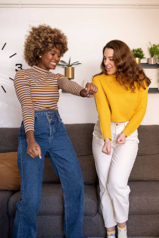 Multiracial young funny women dancing in their apartment. Happy and excited couple of girls celebrating in their living room.