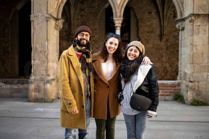 portrait of multiracial group of friends looking at camera. Three happy young adults standing in an ancient city. Holidays, friendship, cheerful concept