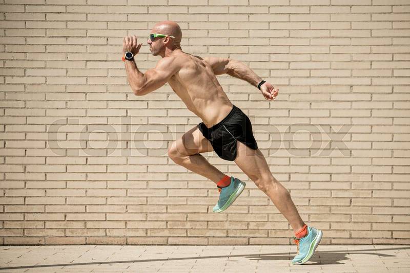 Sideview of a fit athlete running in the street without shirt. Muscular man trainning and sprinting in a city.