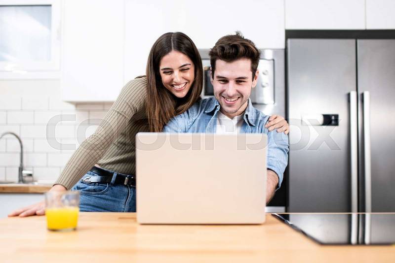 young couple planning vacations together at home looking a laptop. two cheerful young adults sitting on the kitchen. finance concept