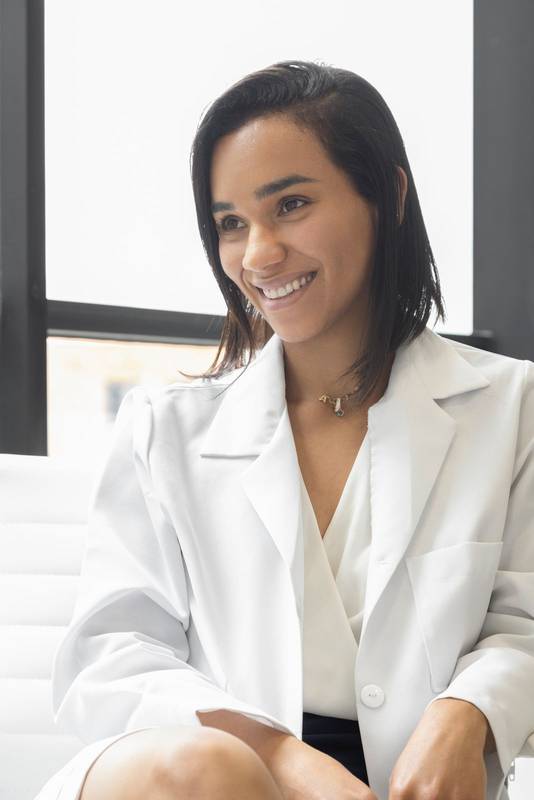 latin female doctor with short hair sitting, smiling and wearing her white uniform coat