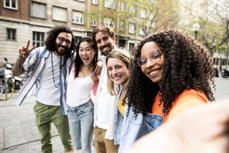 Multiracial group of friends laughing and taking a selfie in the street.Cheerful diverse group of young hipsters taking a picture outside and looking at camera.