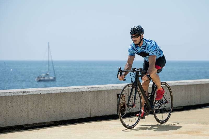 Athletic biker riding a bike in the street next to the sea. Fit cyclist training wearing helmet and sunglasses outdoors.
