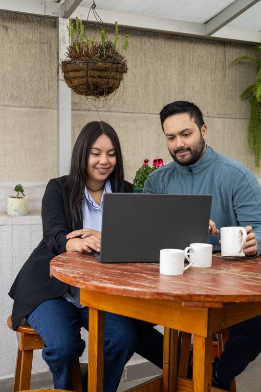 woman and a man stand side by side, looking at a laptop screen and discussing data. The office environment