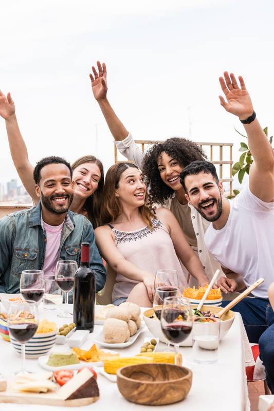 Cheerful multiracial people laughing at rooftop party. Positive group of friends having fun together while having dinner on a terrace.