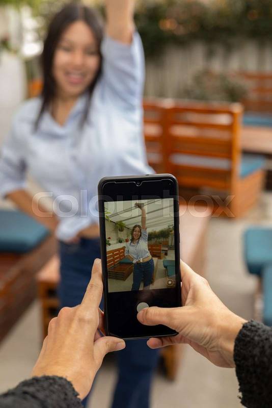 woman smiles warmly as a smartphone camera focuses on her outdoors, blending personal expression, technology