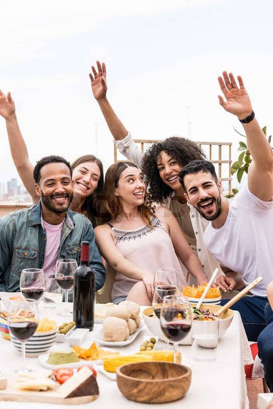 Cheerful multiracial people laughing at rooftop party. Positive group of friends having fun together while having dinner on a terrace.