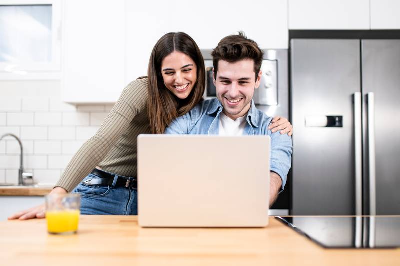 young couple planning vacations together at home looking a laptop. two cheerful young adults sitting on the kitchen. finance concept