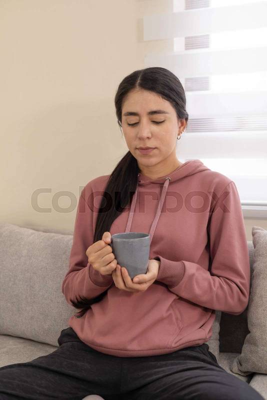 woman sitting on sofa with a cup of coffee in her hands, enjoying a peaceful moment