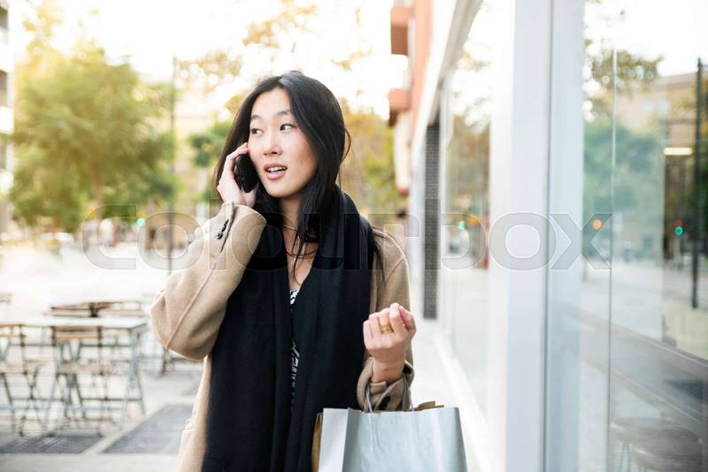 Young woman at the street with shopping bags talking on mobile phone