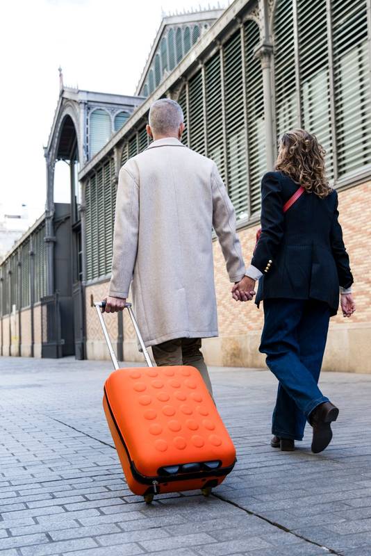 Lovely mid adult tourists couple travelling together walking old town with a suitcase. Romantic senior man and woman walking in a european city in a weekend trip.