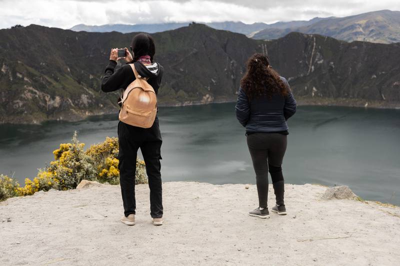 Two women stand side by side on a cliff overlooking a breathtaking landscape