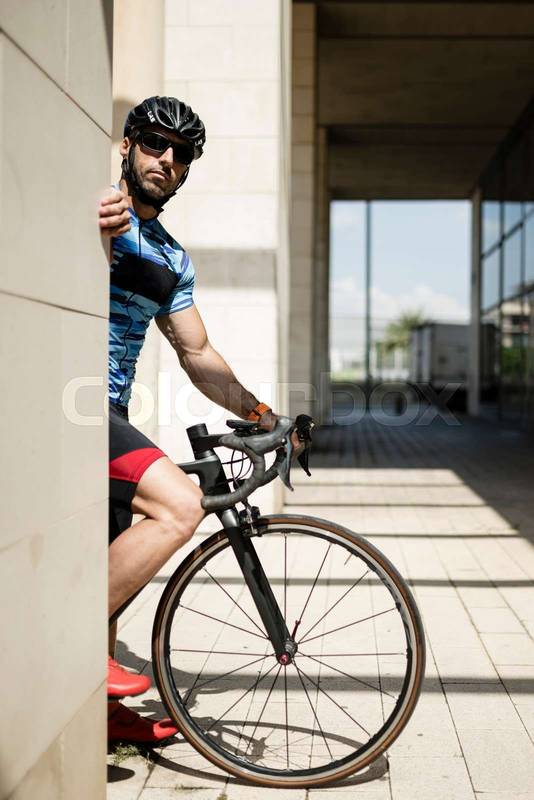 Fit man riding a bike in the city looking at camera. Athletic cyclist male standing on a corner in the street.