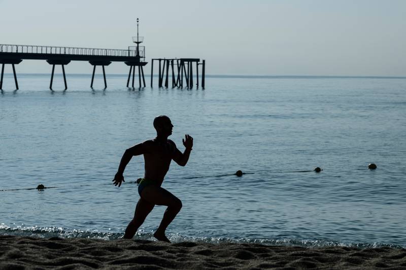 Running man silhouette training at the beach. Athlete jogging next to the sea with a sea dock in background.