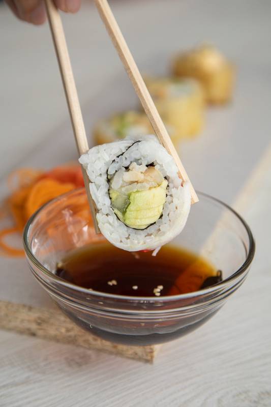 chopsticks holding a sushi roll that is about to be dipped in sauce, healthy prepared food