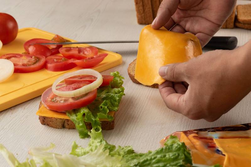 preparing and placing the cheddar cheese of a delicious sandwich with lettuce, fresh tomato and onion rings on a table