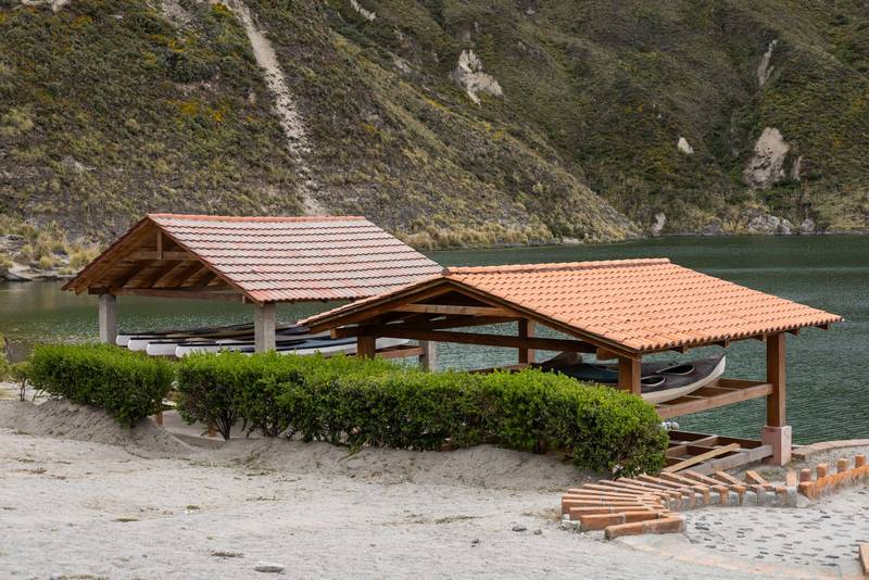 wooden shelters with red tiled roofs stand by a serene lake, nestled among green mountains