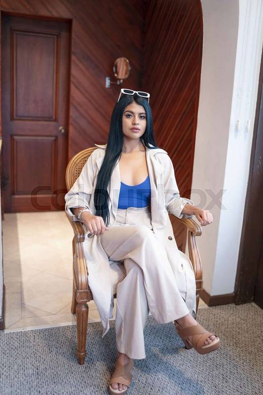 woman sitting resting on a chair, she wears shirt, light clothes and sunglasses