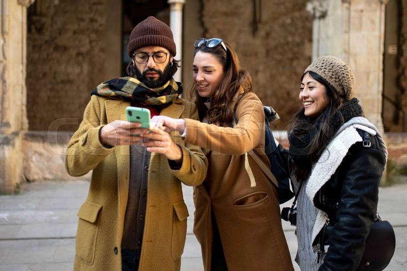 three happy friends using mobile phone on the street at winter. Group of students having fun outside