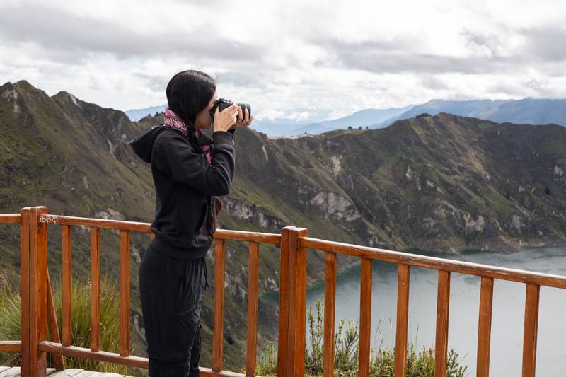 photographing the breathtaking Quilotoa Lake below. The scene evokes creativity, tranquility, photographer