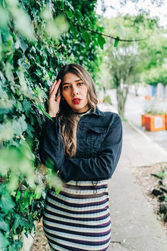 in the city street a young latin woman with long blonde hair, wears makeup with red lips and fashionable clothes