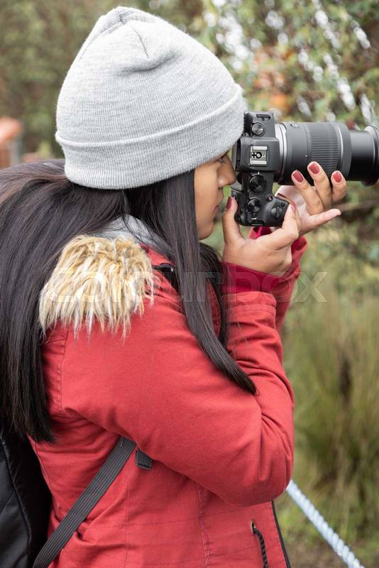 photographer lifestyle in countryside working, young woman in wool cap with long hair holding professional camera