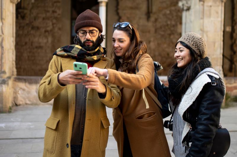 three happy friends using mobile phone on the street at winter. Group of students having fun outside