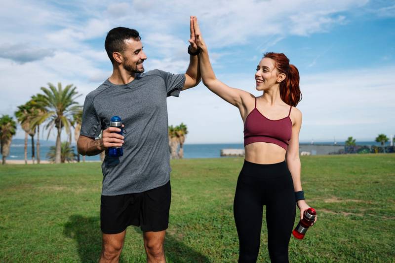 Sport woman and a man high five after a running outside workout. Fitness couple celebrating after successful exercising training outside.