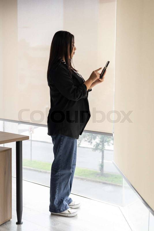 woman in an office reviews her tablet while standing in front of a whiteboard