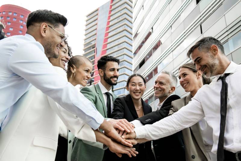 Group of smiling multiethnic businessman and businesswoman holding hands together outside. Multiracial cheerful successful executive team standing in a circle. Teamwork concept.