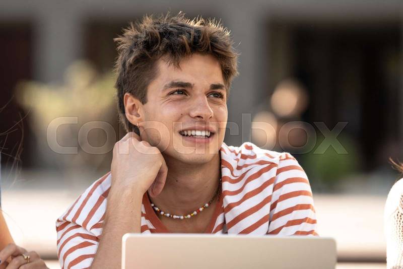 Young handsome hopeful guy smiling.Satisfied teenager sitting with friends smiling and relaxed.