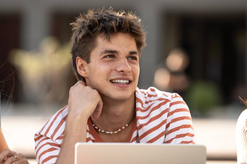 Young handsome hopeful guy smiling.Satisfied teenager sitting with friends smiling and relaxed.