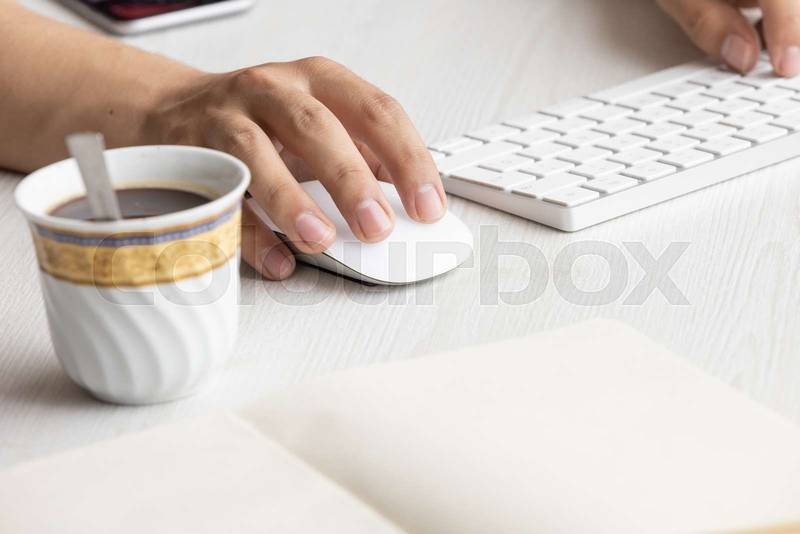 desk with the hands of a person typing on a keyboard and using a mouse