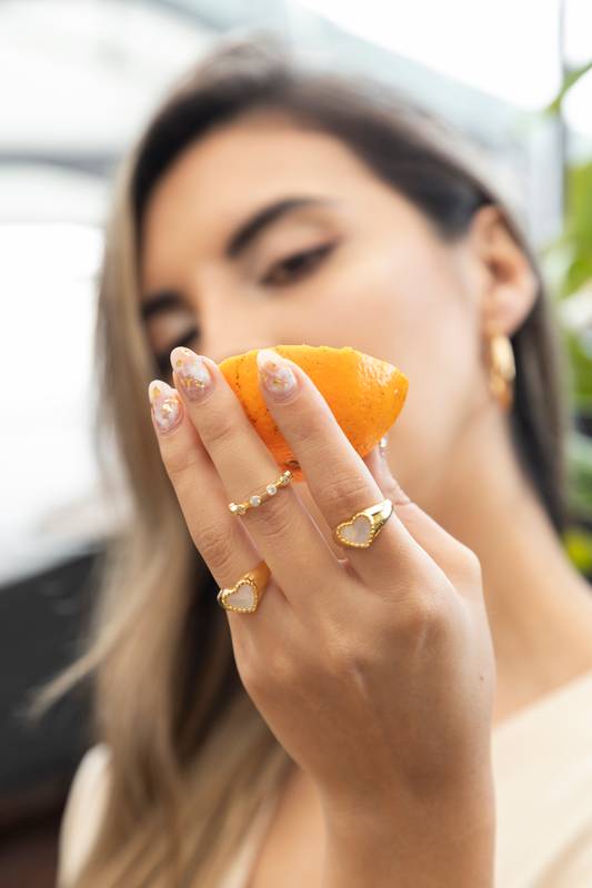 woman holding orange slice, wearing various rings and manicure, fruits and texture detail