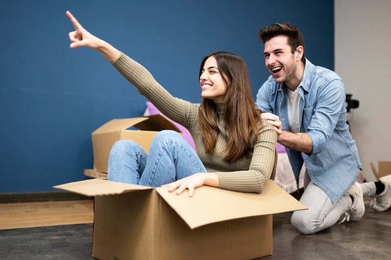 happy young couple having fun with cardboard boxes in new house on moving day. cheerful man and smiling woman unpacking boxes in their new apartment