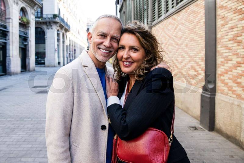 Affectionate senior man and woman hugging happy and relaxed in old town. Lovely mature couple bonding and embracing together looking at camera.
