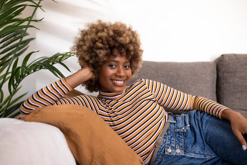 Happy young woman sitting on sofa at home and looking at camera. Portrait of beautiful woman in relaxing on armchair. Portrait of beautiful girl resting and relaxing on couch.