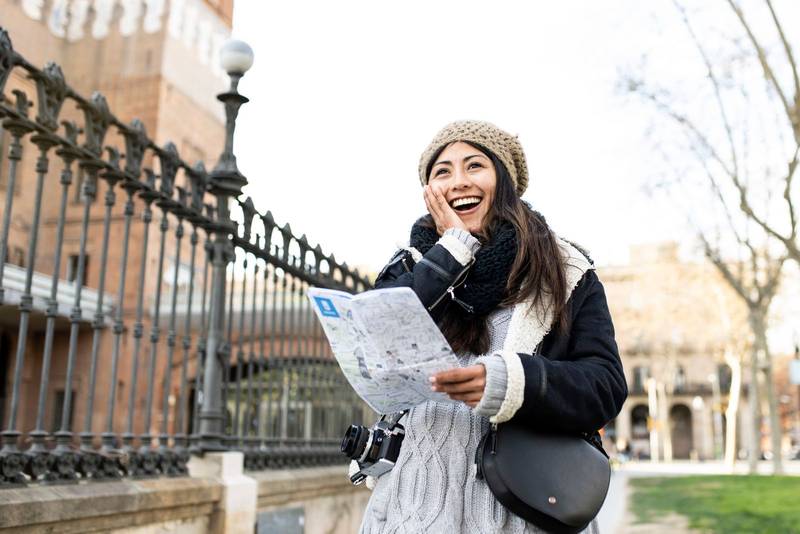 happy young woman surprised holding a map on the city outdoors. Cheerful female smiling when explores her destination on a street travel. Holidays concept