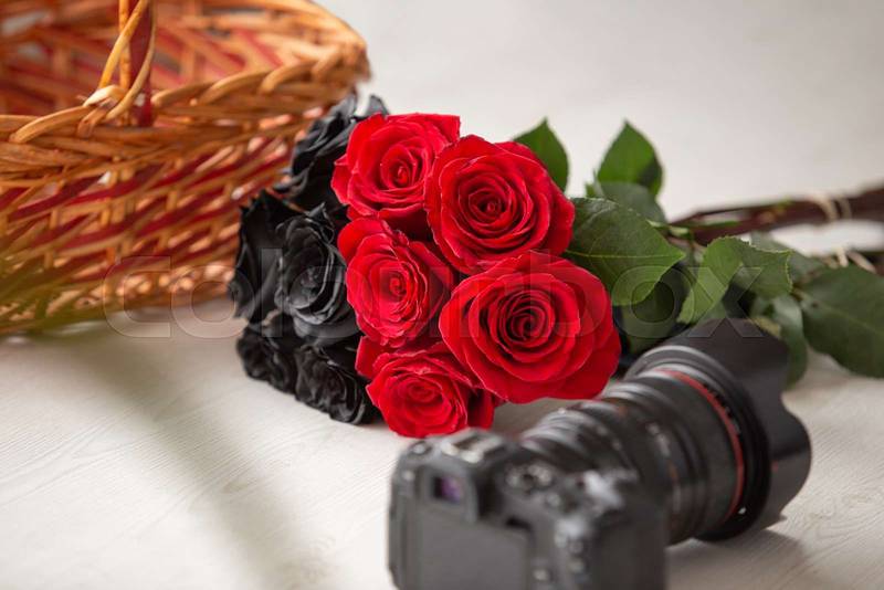 bouquet with black and red roses, next to a modern professional photo camera behind a basket,