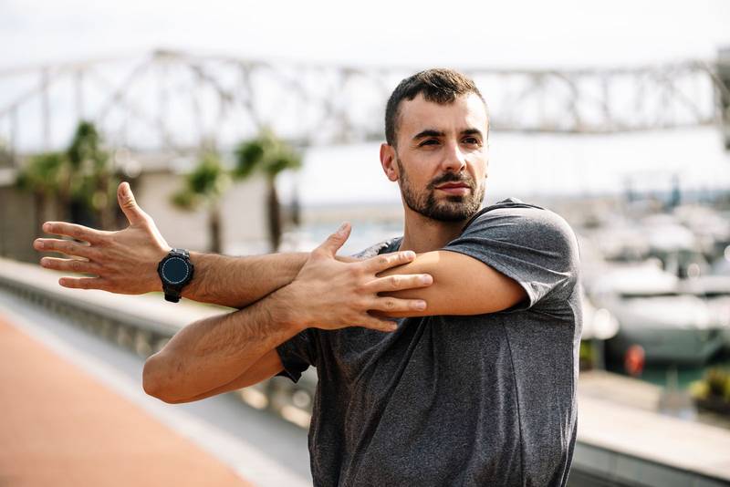 Athlete man stretching before running in the street. Active and sport young male in sportswear warming up for training outside.