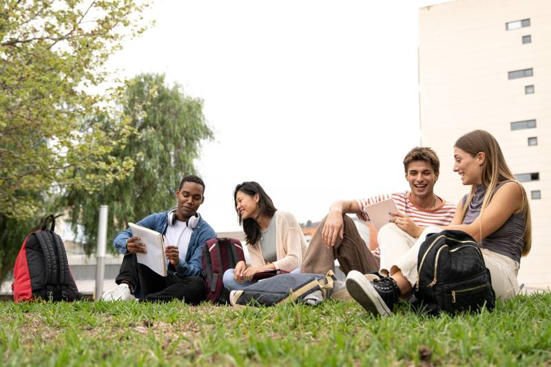 Diverse group of students sitting outside reading documents.Happy multiracial people studying sitting on the floor campus.