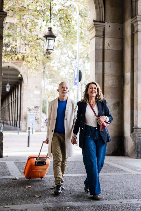 Carefree mid adult tourist couple travelling together visiting Europe city carrying luggage. Laughing senior husband and wife having fun in a weekend romantic trip.