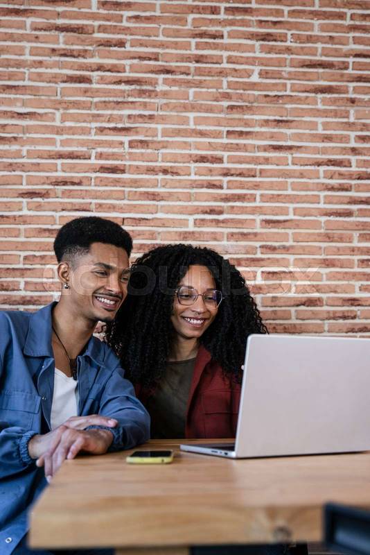 Friendly young adult woman and man in love watching at the computer screen. Happy young diverse couple sitting at living room having laptop video call at home. 