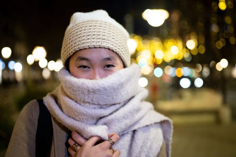 Beautiful young girl wearing knitted hat and scarf at night. Young woman looking at camera during winter standing outdoors