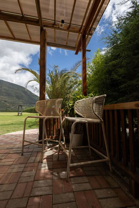 Two wooden country-style chairs placed under a delicate sheer curtain, facing a charming patio surrounded by nature