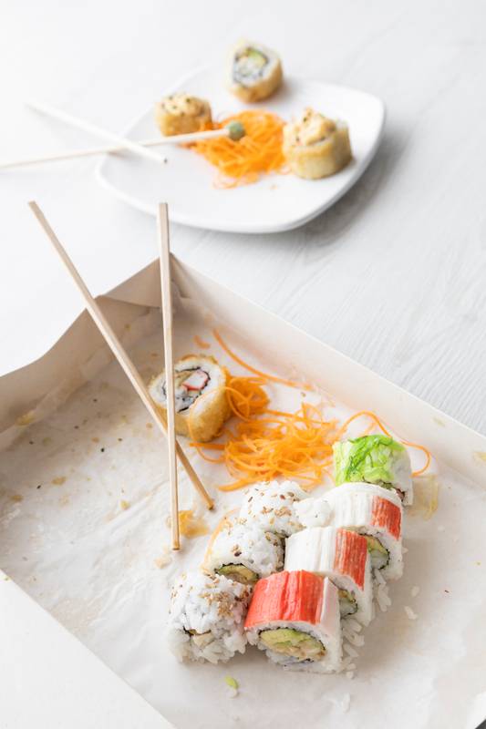 packaging in a cardboard box, with few sushi rolls in a row and some wooden chopsticks