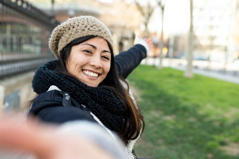 happy woman making a selfie showing two finger in the city. Cheerful portrait of a young female tourist. Holidays, people concept