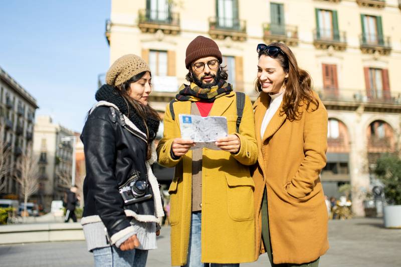 Group of tourists looking a map walking on the street. Three cheerful friends seraching a monument during a city travel